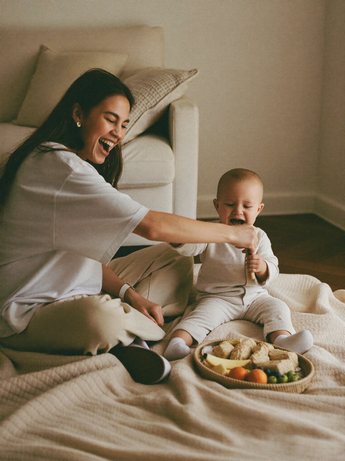 A mum laughing with her baby over a small indoor picnic